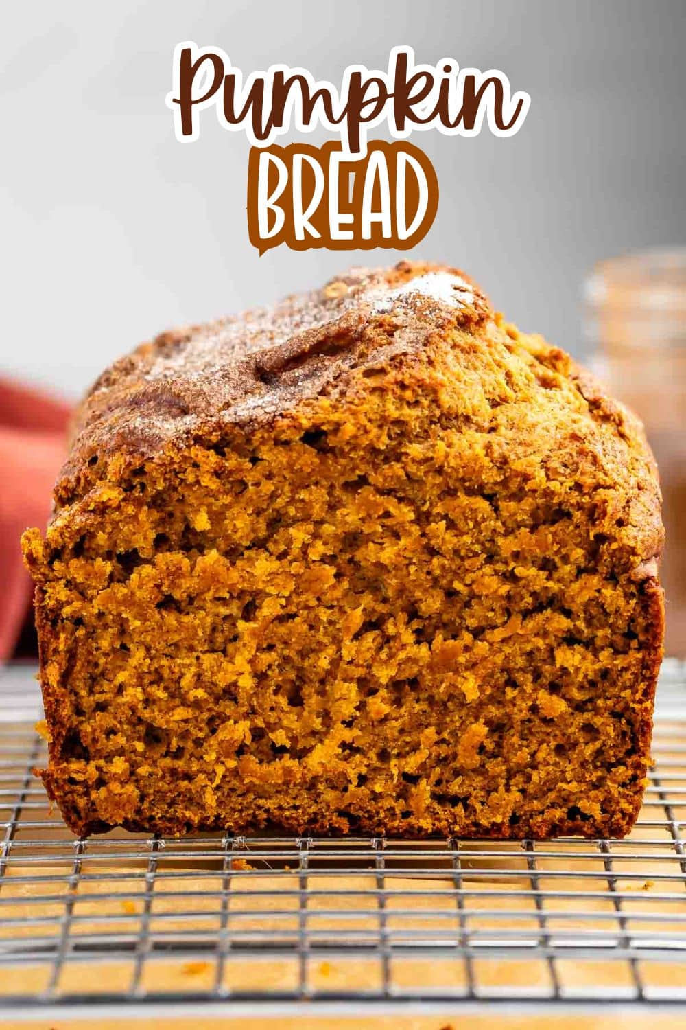 A loaf of pumpkin bread is shown on a cooling rack, sliced to display its moist, orange interior. The text Pumpkin Bread appears at the top of the image in a playful font.