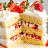 A three-layer cake with white frosting, topped and layered with fresh strawberries. The cake is decorated with whole and sliced strawberries and placed on a round white cake stand.